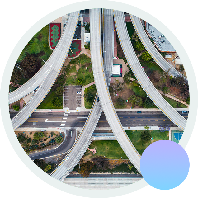 An aerial view of a highway artery branching out over a building, an elementary school, and a park with tennis courts. An aerial view of a highway artery branching out over a building, an elementary school, and a park with tennis courts.
