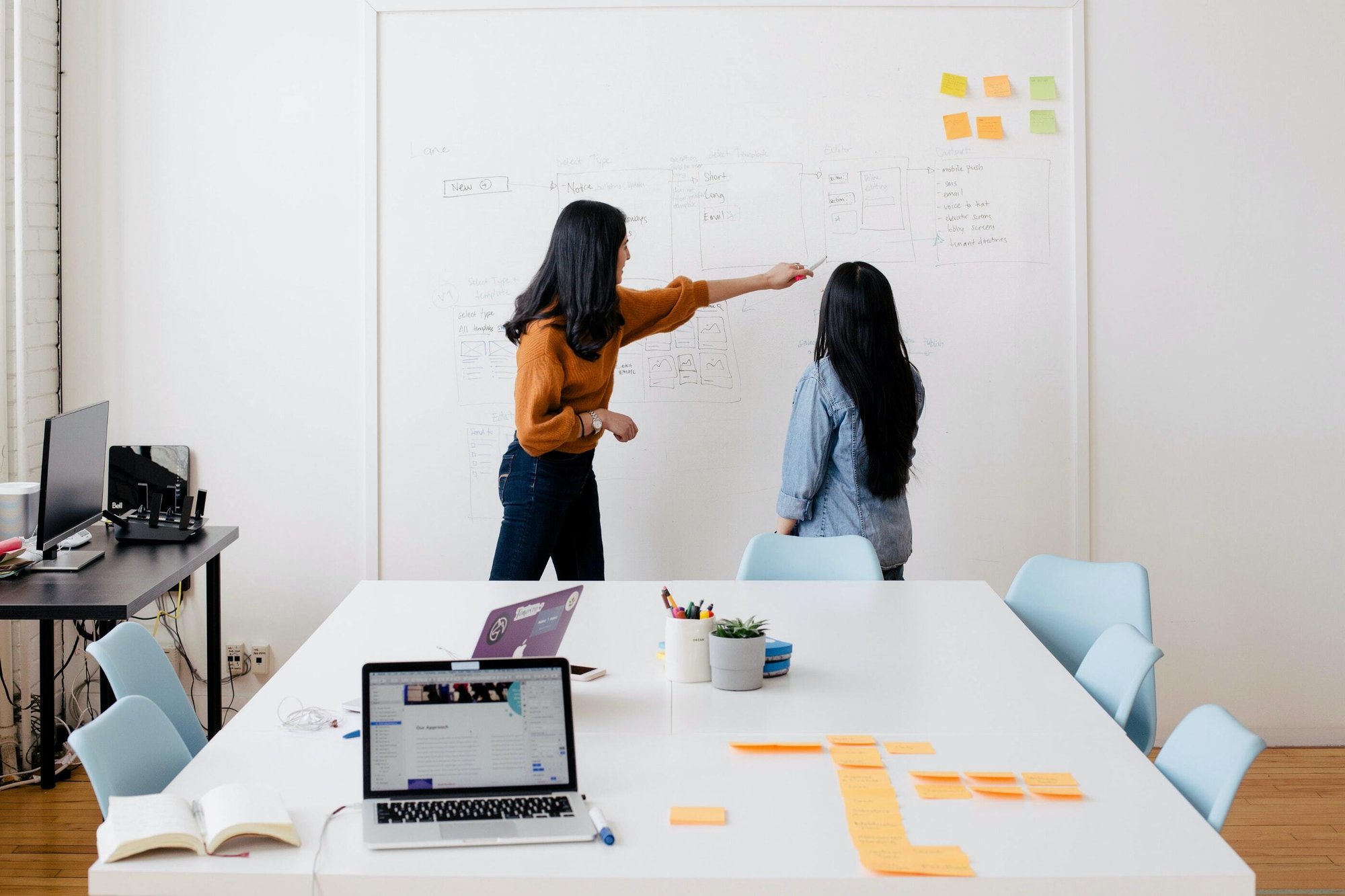 To women discuss a website navigation on a large whiteboard.