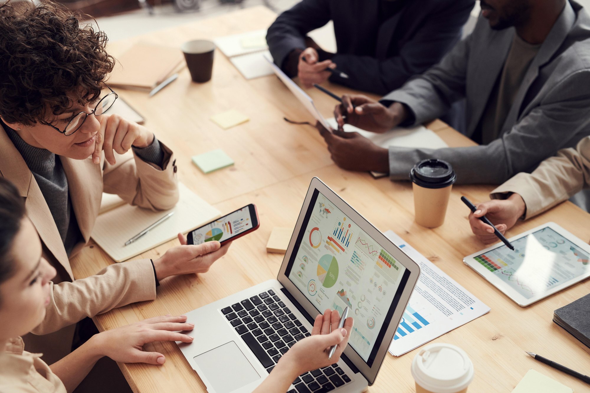 Two women compare analytic data on a laptop screen and phone. Two women compare analytic data on a laptop screen and phone.