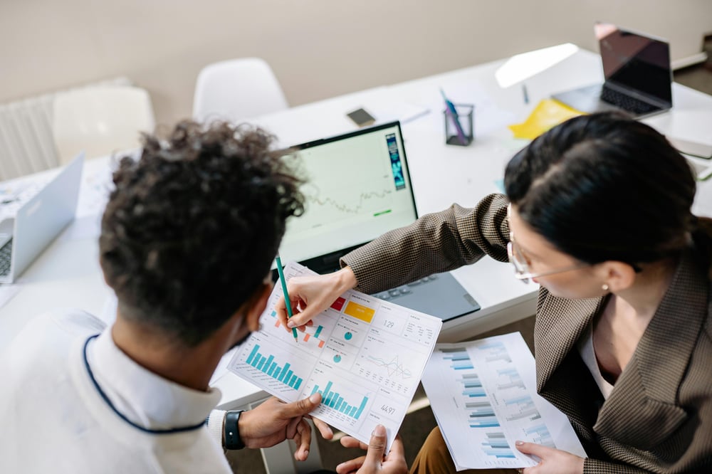 A man and woman investigate pages of graphs and charts. A man and woman investigate pages of graphs and charts.