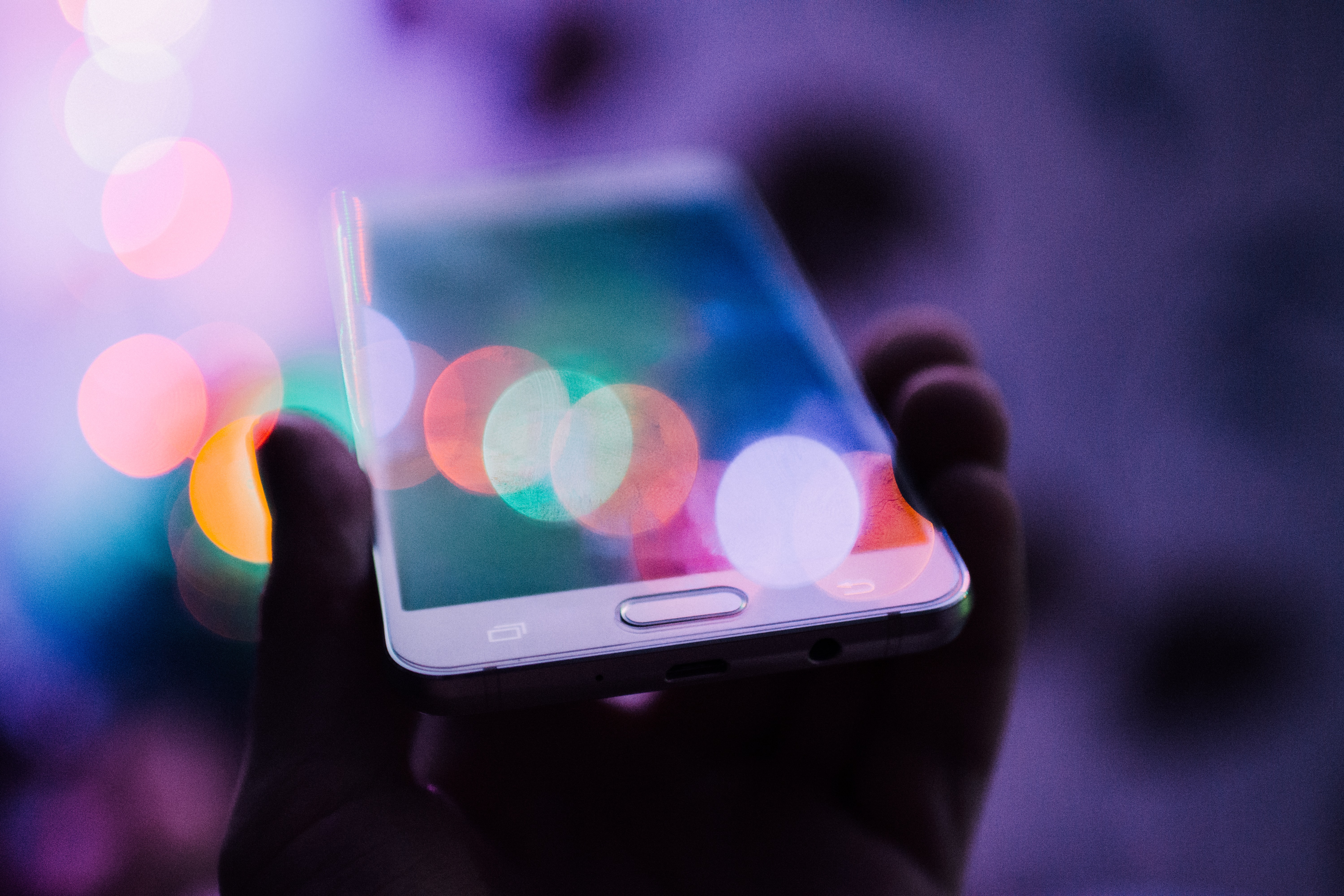 Person Holding a Mobile Phone In Bokeh Lighting