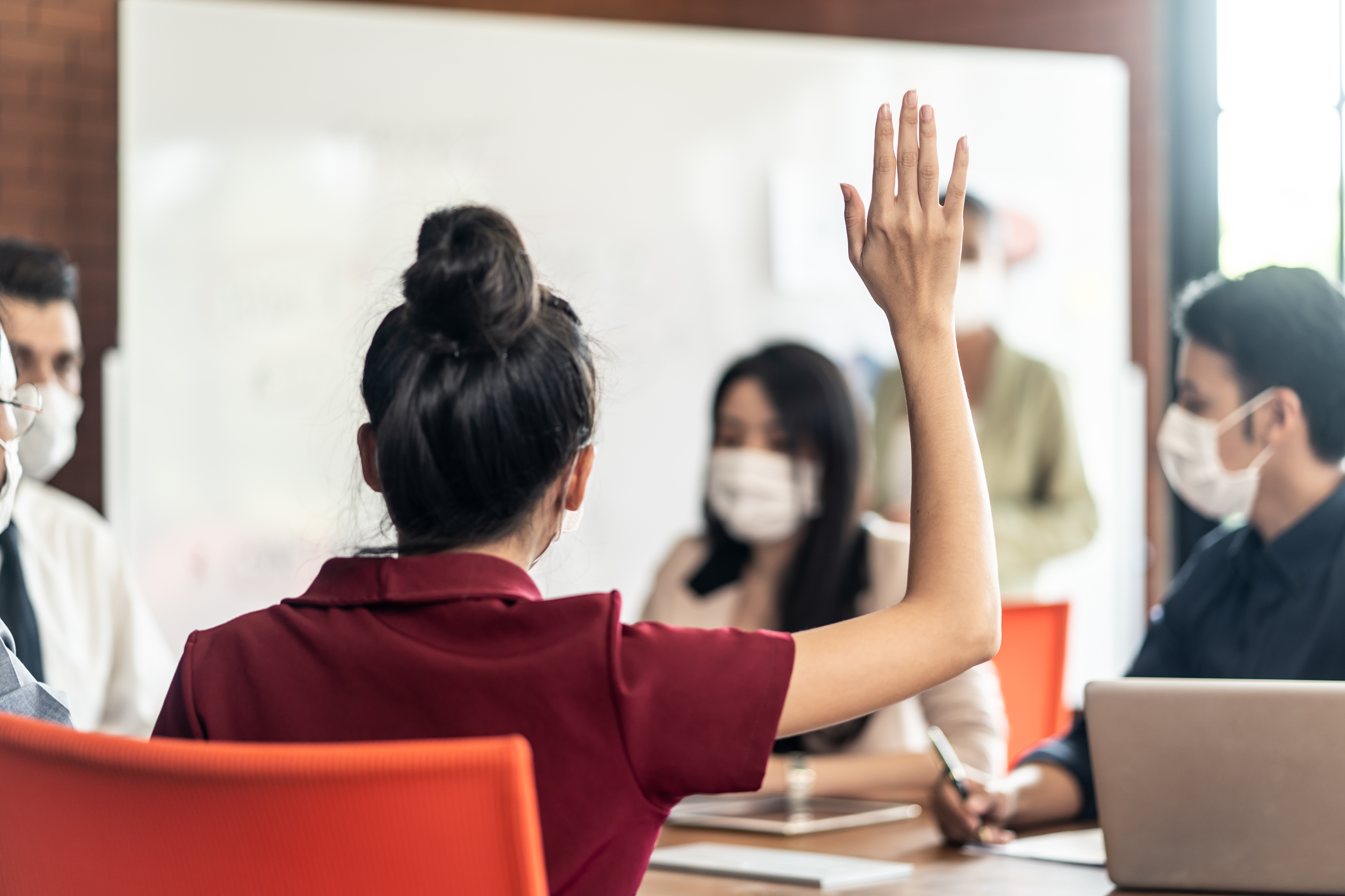 Focus on raising hand of young woman having question in group brainstorm in an office. 